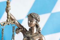 Bild zeigt Justitia vor blau-weißen Rautenhintergrund 